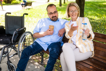 Man in wheelchair is spending time with his mother in park. - 785111277