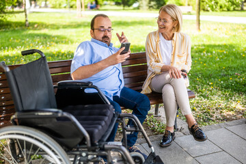 Man in wheelchair is spending time with his mother in park. - 785111289