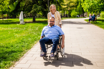 Man in wheelchair is spending time with his mother in park. They are enjoying sunny day together.