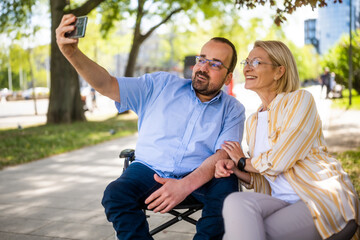 Man in wheelchair is spending time with his mother in park. They are taking selfie. - 785111620