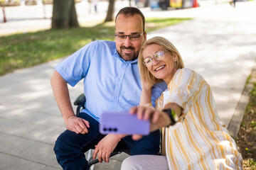 Man in wheelchair is spending time with his mother in park. They are taking selfie. - 785111628
