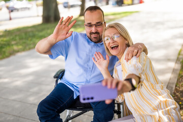 Man in wheelchair is spending time with his mother in park. They are taking selfie. - 785111655