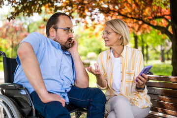 Man in wheelchair is spending time with his mother in park. - 785111658