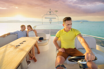 Luxury traveling and vacation. Group of  people sitting on the yacht deck sailing the sea. Young handsome man driving sailboat on sunset