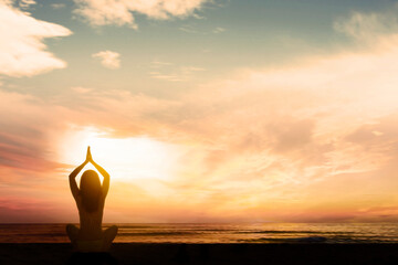 Silhouette of young woman exercising yoga while doing meditation at beach