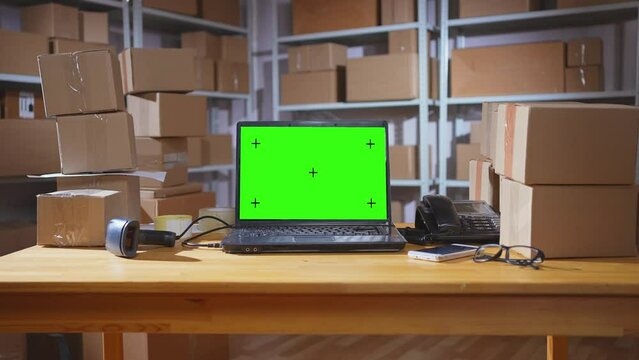 zoom in laptop with a green screen on the background of a warehouse with boxes shipping company