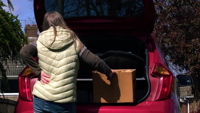 Woman with bad back injury moving box from car trunk