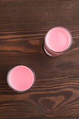 Sweet strawberry liqueur in glass on a brown wooden. top view, flat lay.