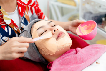 Beautiful young Asian woman getting a facial mask treatment at the beauty salon. Facial skincare.