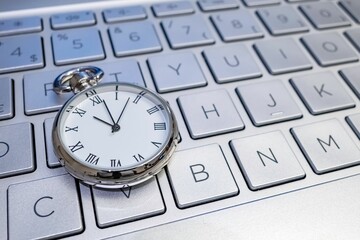 Close up beautiful shot of pocket silver clock with white dial on laptop keyboard