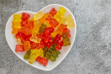 Closeup of colorful jelly beans in the heart figured white plate on gray surface