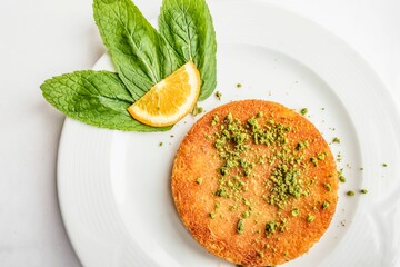 Top view of Kunefe sweet cheese pastry from Turkish cuisine served on white plate with orange slice