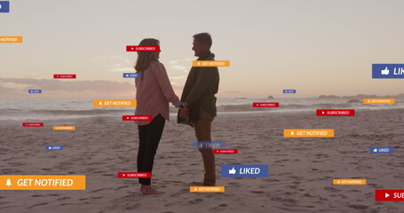 Image of social media text and icons over caucasian couple on beach