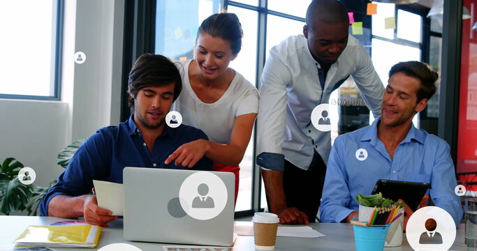 Image of profile icons over diverse coworkers discussing reports on laptop and digital tablet