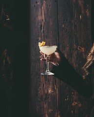 Vertical shot of human hand holding a glass of summer babe cocktail against dark wooden background