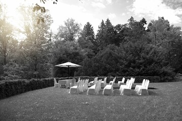 Grayscale of a wedding altar with white chairs and a parasol in a summer garden