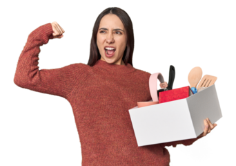 Caucasian young woman holding a box for moving on studio background raising fist after a victory, winner concept.