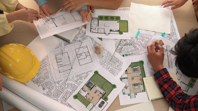 Architect and safety engineer discussion about building construction use blueprint on table with architectural document, measurement tool and wooden block scatter around at modern office. Delineation.
