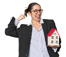 Caucasian businesswoman with house model, real estate concept on studio background raising fist...