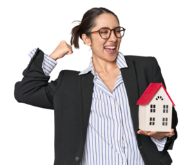 Caucasian businesswoman with house model, real estate concept on studio background raising fist after a victory, winner concept.