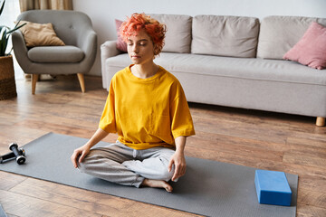 attractive extravagant queer person with red hair in vibrant yellow t shirt meditating at home
