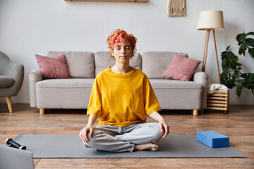 attractive extravagant queer person with red hair in vibrant yellow t shirt meditating at home