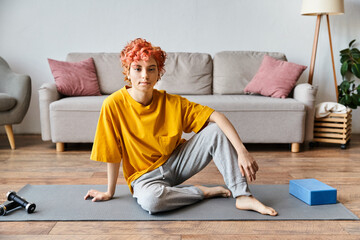 beautiful queer person in vibrant yellow t shirt sitting on yoga mat and looking at camera