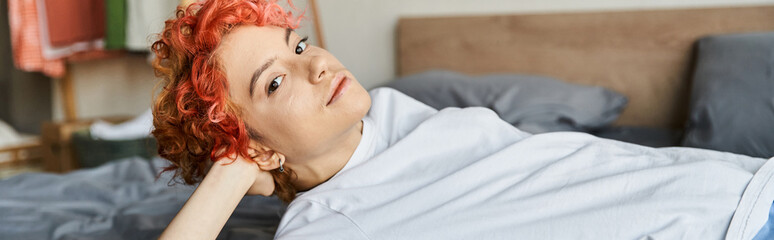 appealing queer person with red hair lying on her bed and looking at camera, leisure time, banner