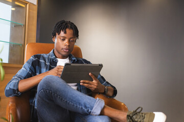 African American man sitting in a modern business office, using tablet with copy space