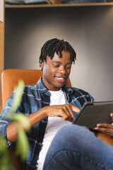 African American man sitting in a modern business office, using a tablet with a smile