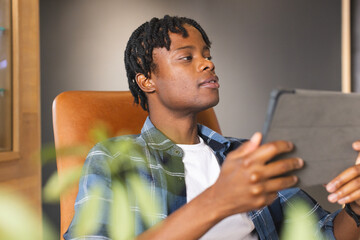 African American man holding tablet, looking at screen in a modern business office