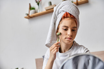 attractive jolly queer person in homewear using face roller in front of mirror as morning routine