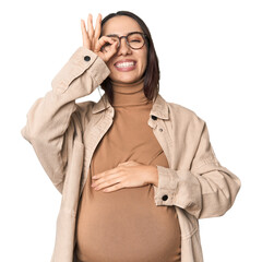 Pregnant young Caucasian woman showcasing maternity on studio background excited keeping ok gesture...