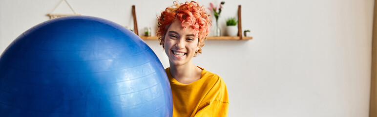 joyous queer person in comfy attire exercising with fitness ball and smiling at camera, banner