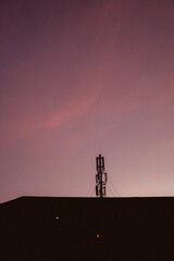 Naklejka premium Vertical shot of a base station on top of the apartment building against the magenta sunset sky