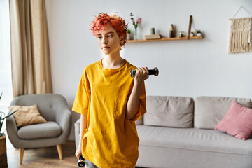 attractive young queer person in vibrant sport attire exercising with dumbbells while at home