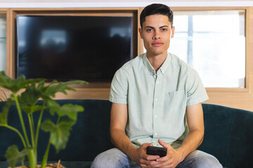 A young biracial man holding a smartphone sits on a couch in a modern business office
