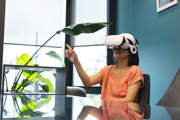A young Asian woman wearing VR headset is pointing at something in a modern business office