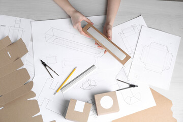 Woman creating packaging design at light wooden table, top view