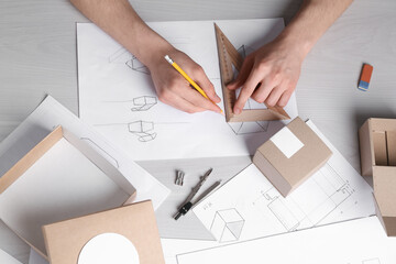 Man creating packaging design at light wooden table, top view