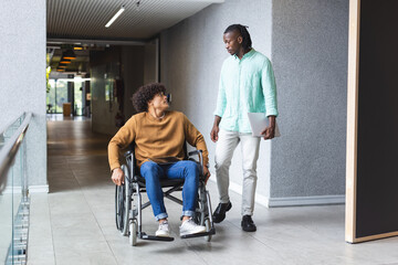 African American man walking beside biracial man in wheelchair in a modern business office - Powered by Adobe