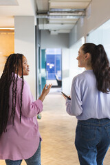 Biracial woman talking with Caucasian woman, both standing in a modern business office