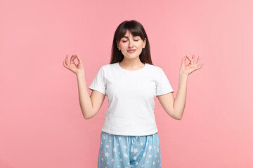 Woman in pyjama meditating on pink background