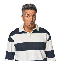 Middle-aged Latino man shrugs shoulders and open eyes confused.