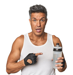 Gym-ready Hispanic man with water bottle pointing to the side