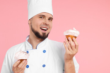 Happy professional confectioner in uniform holding delicious cupcakes on pink background