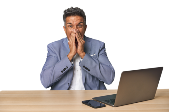 Elegant businessman at desk with laptop shouting excited to front.
