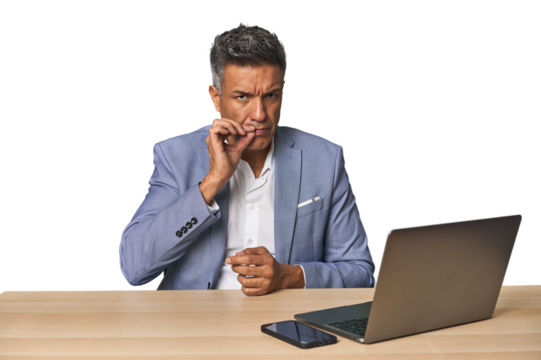 Elegant businessman at desk with laptop with fingers on lips keeping a secret.
