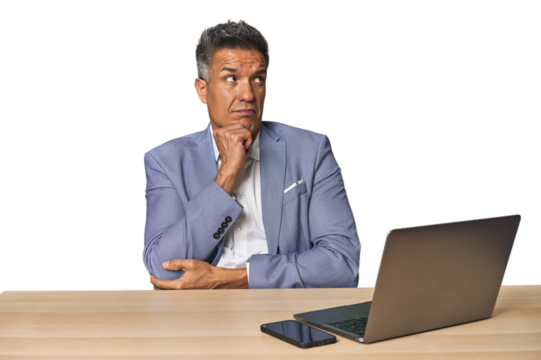 Elegant businessman at desk with laptop thinking and looking up, being reflective, contemplating, having a fantasy.