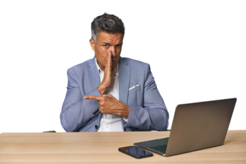 Elegant businessman at desk with laptop saying a gossip, pointing to side reporting something.